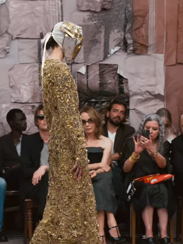 Maison Margiela 以回收金屬盒、舊皮衣、廢棄布料等材料，耗費數百小時手工縫製出宛如金甲鎧甲般的高訂禮服，重新定義時尚奢華。由創意總監 Glenn Martens 領軍，品牌堅持永續且不妥協的設計哲學，在巴黎Le Centquatre地點舉行的2025秋冬高訂大秀，以匿名的金屬面罩呈現，完美展現品牌反奢華精神與創造力煉金術。此一系列不以物料價格衡量奢華，而在於將廢棄物料轉化為獨一無二的藝術作品，延續Maison Margiela經典的永續時尚理念。