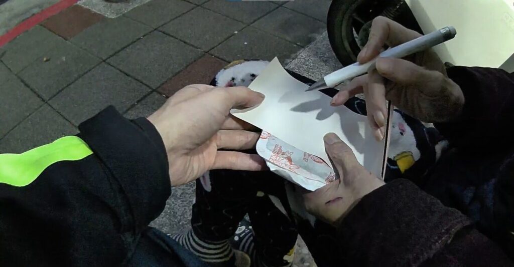 「寒夜迷途」坐路旁 內湖暖警伸援助長者返家 員警嘗試讓老翁書寫名字。(圖/記者薛秀蓮 翻攝)