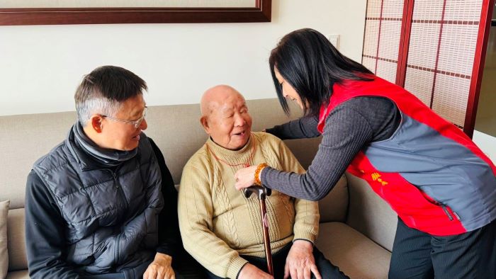 新北榮服處暖訪中和百歲榮民 長輩開心讚「Very Good」 11 《圖說》王玟琳組長(右)代表致贈金壽桃,親自為郭爺爺(中)戴上,向郭爺爺祝賀壽誕。〈新北榮服處提供〉