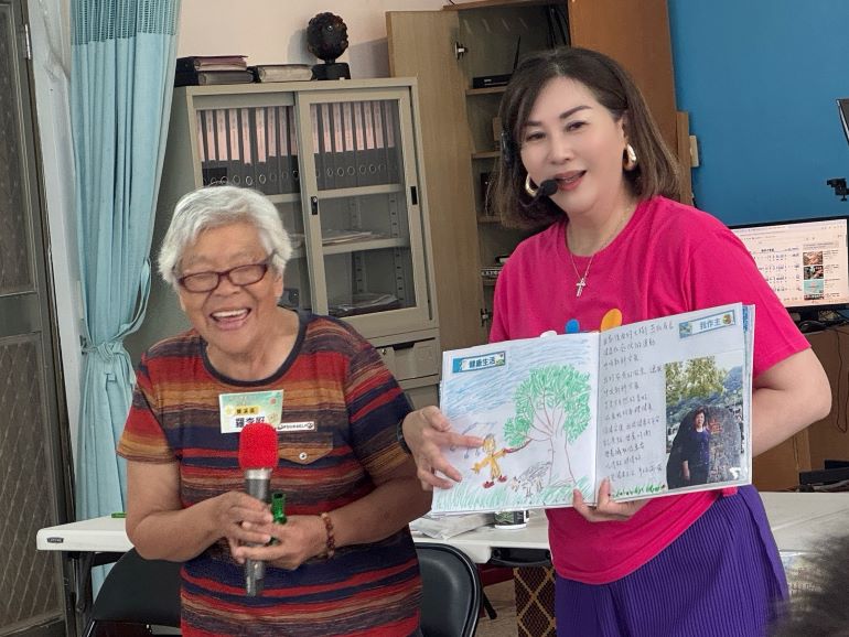 八旬長輩畫出人生彩虹 阿公〈我愛你〉阿嬤羞紅臉 13 《圖說》羅李屘阿嬤(左)在生命繪本中畫出里長幫忙鋸家門前的大樹。〈社會局提供〉