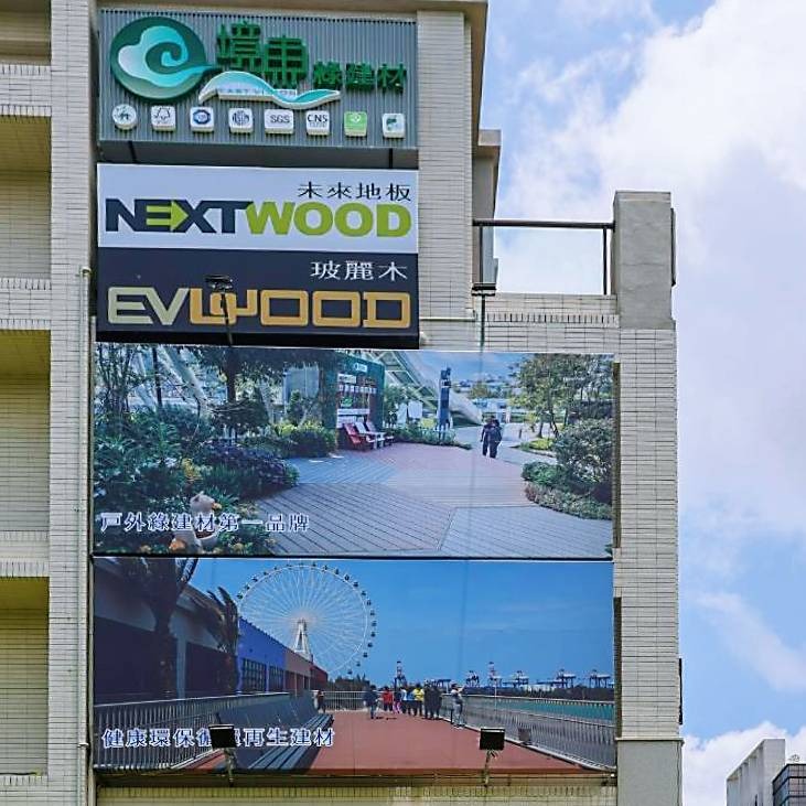 海風吹了八年也吹不壞:境東綠建材用回收木粉造塑木,把25年減碳承諾釘進台灣地標 境東台中總部大樓外牆懸掛品牌看板與工程實績照片,標示「戶外綠建材第一品牌」與「健康環保循環再生建材」,展現品牌市場定位。圖:境東綠建材提供